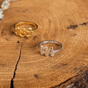 以下が含まれることがあります： 木製の表面に置かれた2つの金の指輪。指輪はどちらも数字の4の形をしています。1つは金、もう1つは銀です。