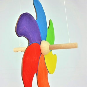 Könnte beinhalten: Ein bunter Holz-Windfänger mit sechs Flügeln in den Farben Lila, Blau, Grün, Gelb, Orange und Rot. Der Windfänger ist an einer weißen Schnur aufgehängt und hat eine Holzstange.