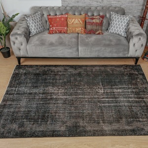 May include: A black and gray vintage-style rug with a distressed look. The rug is laid out on a wooden floor in front of a gray sofa with pillows.