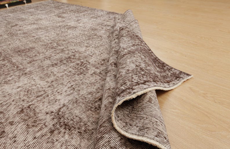 May include: A rolled-up, distressed-look rug with a faded brown and beige color palette. The rug's texture is visible, with a pattern of lines and subtle variations in tone. The edges of the rug are frayed, adding to its vintage aesthetic.