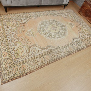 May include: A rectangular, peach-colored area rug with an intricate floral pattern. The rug features a central medallion design and ornate borders in shades of cream, brown, and yellow. The rug is placed on a light-colored wooden floor.
