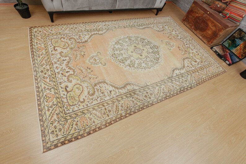May include: A rectangular, peach-colored area rug with an intricate floral pattern. The rug features a central medallion design and ornate borders in shades of cream, brown, and yellow. The rug is placed on a light-colored wooden floor.
