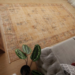 May include: A vintage-style rug with a faded, light brown background and a floral pattern in shades of blue, red, and orange. The rug has a distressed look and is laid out on a wooden floor.