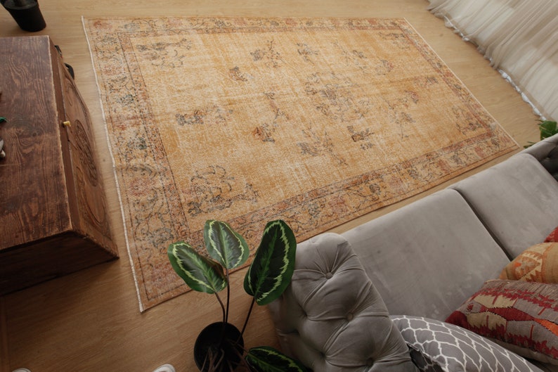 May include: A vintage-style rug with a faded, light brown background and a floral pattern in shades of blue, red, and orange. The rug has a distressed look and is laid out on a wooden floor.