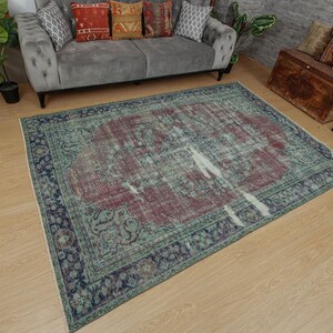 May include: A rectangular area rug featuring a large central medallion in deep red surrounded by a faded sage green field. The border is dark blue with intricate floral patterns. The rug has a distressed, weathered appearance throughout.