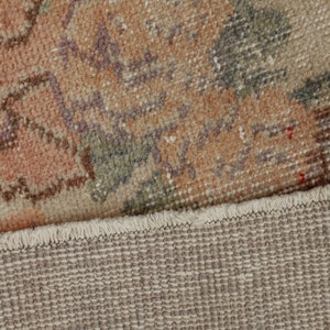 May include: Close-up of the back side of a rug with a floral pattern. The rug has a fringe border and a woven backing.