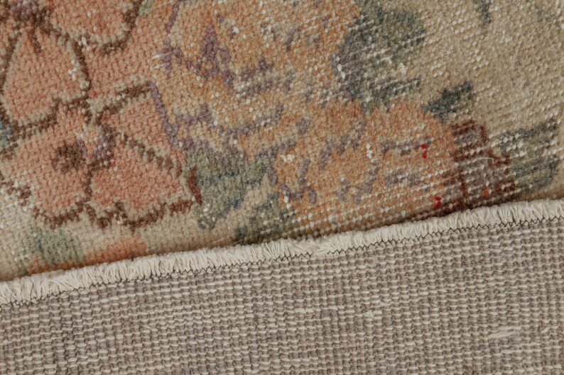 May include: Close-up of the back side of a rug with a floral pattern. The rug has a fringe border and a woven backing.