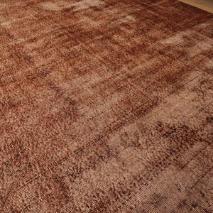 May include: A large rectangular area rug featuring a deep, monochromatic rust-brown color palette. The surface displays a distressed, weathered texture with visible woven fibers and subtle variations in tone across the entire flat textile.