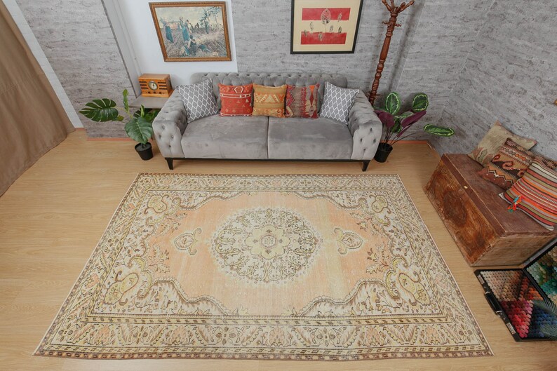 May include: A large, rectangular area rug with an intricate, traditional design. The rug features a central medallion in cream and peach tones, surrounded by a border with floral and geometric patterns in shades of brown, beige, and yellow. The rug is placed on a wooden floor.