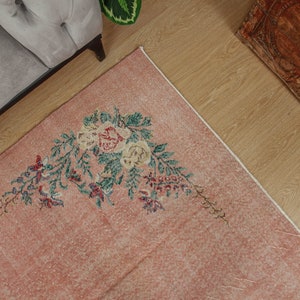 May include: A pink vintage rug with a floral design featuring green leaves and pink and white flowers. The rug has a distressed look and is perfect for adding a touch of vintage charm to any room.
