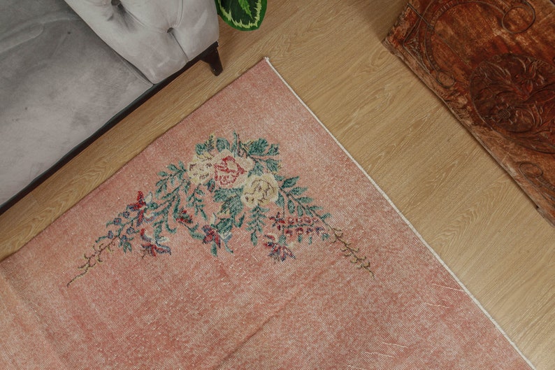 May include: A pink vintage rug with a floral design featuring green leaves and pink and white flowers. The rug has a distressed look and is perfect for adding a touch of vintage charm to any room.