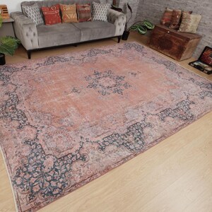 May include: A large rectangular area rug featuring a faded peach and salmon-colored center with a dark blue floral medallion. The border displays intricate dark blue and muted pink botanical patterns, creating a distressed, weathered appearance.