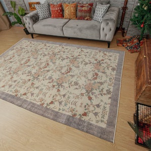 May include: A cream-colored rug with a floral pattern and a gray border. The rug is on a wooden floor in a living room setting.