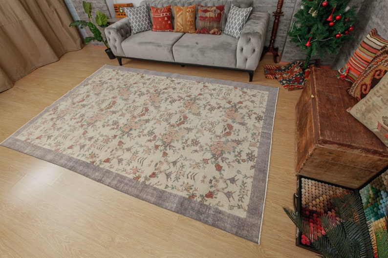 May include: A cream-colored rug with a floral pattern and a gray border. The rug is on a wooden floor in a living room setting.