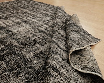 Pode incluir: Um tapete preto e branco com um aspeto envelhecido. O design do tapete apresenta um padrão texturizado, com uma parte enrolada, revelando a parte inferior. O tapete é feito de um material tecido.