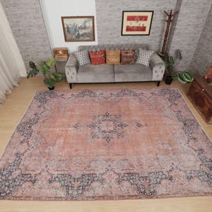 May include: A large rectangular area rug featuring a faded peach and terracotta base color with a dark blue intricate floral and geometric border pattern. The center of the rug displays a matching dark blue medallion design on a textured surface.