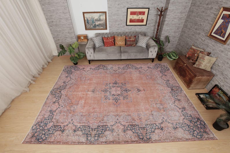 May include: A large rectangular area rug featuring a faded peach and terracotta base color with a dark blue intricate floral and geometric border pattern. The center of the rug displays a matching dark blue medallion design on a textured surface.