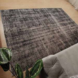 May include: A rectangular area rug featuring a distressed, mottled pattern in shades of charcoal grey, black, and off-white. The rug has a low-pile texture with a faded, weathered appearance across its entire surface, showcasing a neutral colour palette.