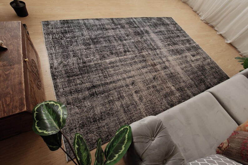 May include: A rectangular area rug featuring a distressed, mottled pattern in shades of charcoal grey, black, and off-white. The rug has a low-pile texture with a faded, weathered appearance across its entire surface, showcasing a neutral colour palette.