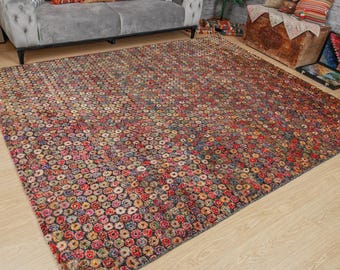 May include: A large, rectangular area rug with a dense pattern of small, colorful circles in shades of red, pink, blue, and yellow. The rug has a dark background and is placed on a light-colored wooden floor. The rug is in a living room setting.