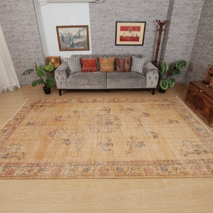 May include: A light beige area rug with a floral pattern and a faded, vintage look. The rug has a dark brown border with a floral design. The rug is laid out on a wooden floor in a living room setting.
