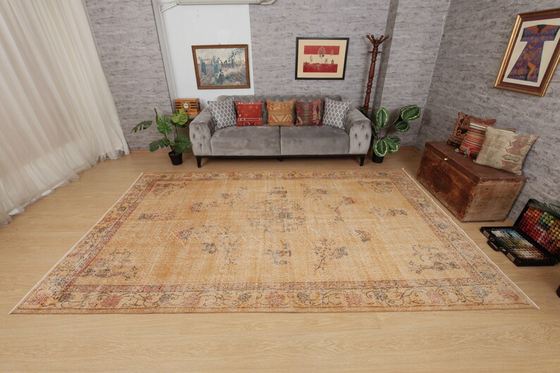 May include: A light beige area rug with a floral pattern and a faded, vintage look. The rug has a dark brown border with a floral design. The rug is laid out on a wooden floor in a living room setting.