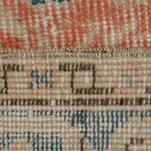 Puede incluir: Primer plano del borde tejido de una alfombra con un patr&oacute;n beige, marr&oacute;n y azul.