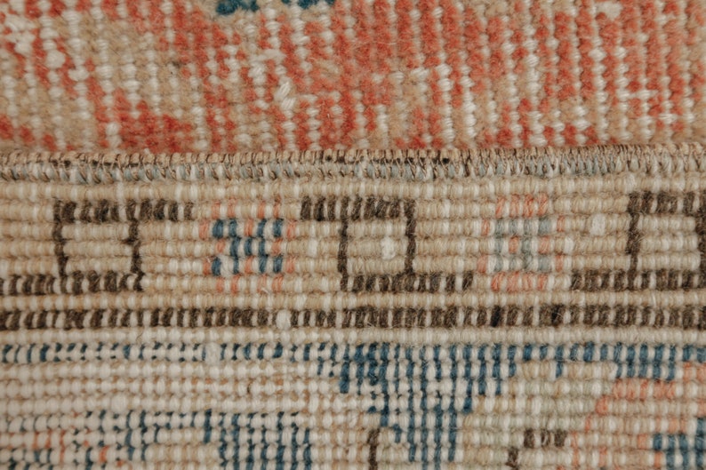 Puede incluir: Primer plano del borde tejido de una alfombra con un patr&oacute;n beige, marr&oacute;n y azul.