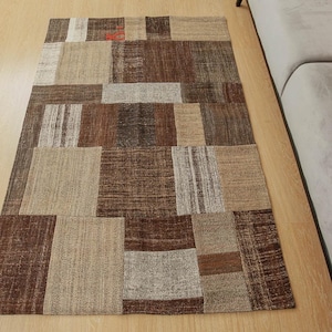 May include: A brown and beige patchwork rug with a variety of textures and patterns. The rug is made of woven fabric and has a rectangular shape.