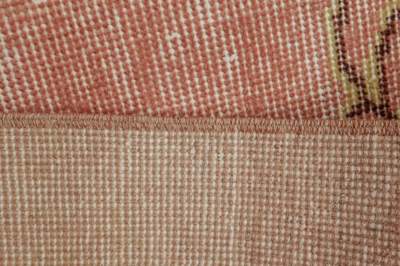 May include: Close-up of a rug with a pink and white patterned top and a beige bottom. The rug has a woven texture.