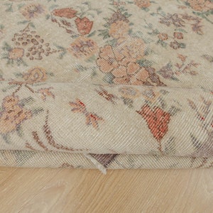 May include: A close-up of a rolled-up beige rug with a floral pattern. The rug has a subtle, faded look, giving it a vintage feel.