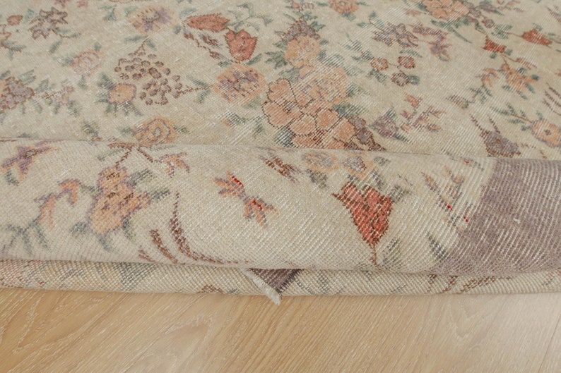 May include: A close-up of a rolled-up beige rug with a floral pattern. The rug has a subtle, faded look, giving it a vintage feel.