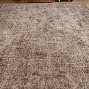 May include: A large, rectangular rug with a distressed, vintage appearance. The rug features a faded, mottled pattern in shades of brown and beige, creating a soft, textured look. The design includes subtle floral or geometric motifs.