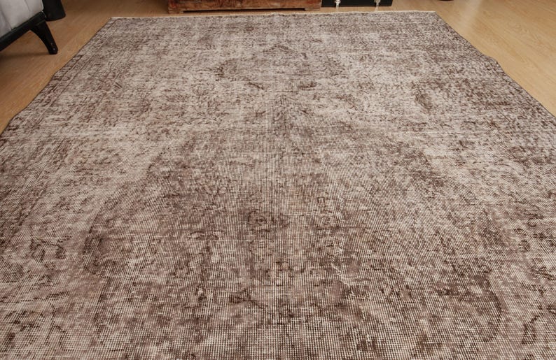 May include: A large, rectangular rug with a distressed, vintage appearance. The rug features a faded, mottled pattern in shades of brown and beige, creating a soft, textured look. The design includes subtle floral or geometric motifs.