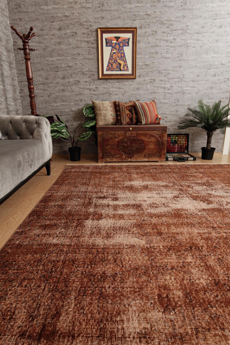 May include: A large rectangular area rug featuring a distressed, weathered texture in shades of deep rust, terracotta, and faded cream. The rug has a low-pile construction with a visible woven grid pattern, covering the floor space in front of a sofa.