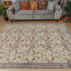 May include: A cream-colored rug with a floral pattern in shades of pink, brown, and green. The rug has a dark gray border.