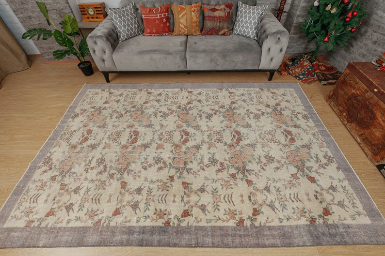 May include: A cream-colored rug with a floral pattern in shades of pink, brown, and green. The rug has a dark gray border.