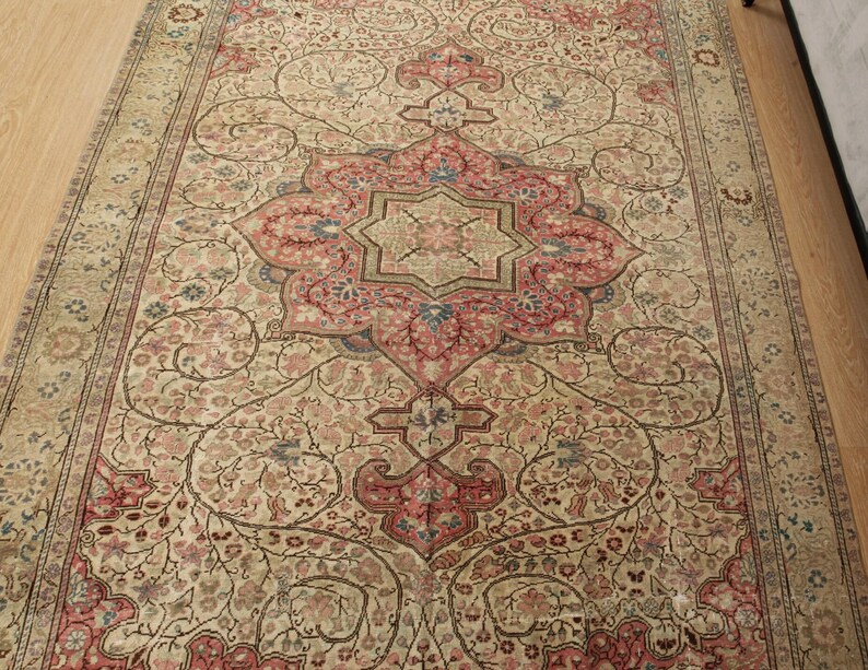 Pu&ograve; includere: Un tappeto rettangolare con un intricato motivo floreale in crema, rosso e blu. Il disegno centrale presenta un grande medaglione ornato a forma di stella. Il bordo del tappeto presenta un motivo floreale ripetuto.