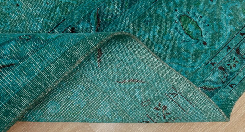 May include: Close-up of the back side of a teal blue rug with a woven pattern. The rug is folded in half, showing the texture of the fabric.