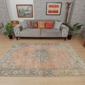 Puede incluir: Una alfombra de estilo vintage con un esquema de color naranja y crema descolorido. La alfombra tiene un patr&oacute;n floral detallado en el centro y un borde azul.