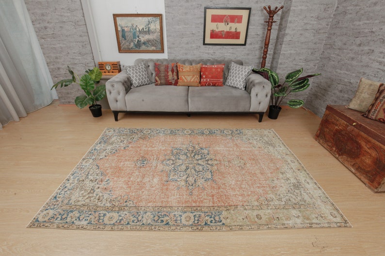 Puede incluir: Una alfombra de estilo vintage con un esquema de color naranja y crema descolorido. La alfombra tiene un patr&oacute;n floral detallado en el centro y un borde azul.