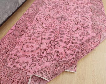 May include: A pink vintage rug with an intricate floral and paisley design. The rug features a central medallion and border in shades of pink and brown. The rug is partially rolled up, revealing its underside.