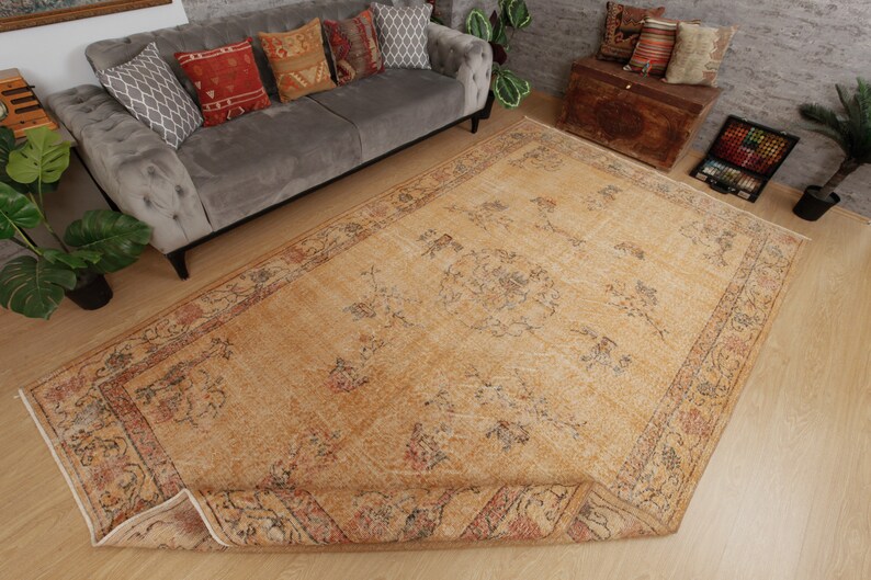 May include: A vintage-style rug with a beige background and a floral pattern in shades of brown, red, and blue. The rug has a fringed edge and is laid out on a wooden floor.