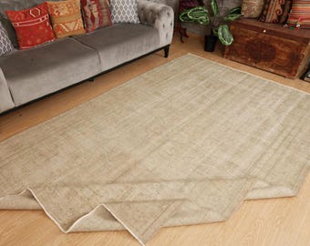 May include: A large, rectangular beige rug with a distressed, vintage appearance. The rug is laid out on a wooden floor, with a rolled-up edge. The rug is a neutral colour and would complement various interior design styles.