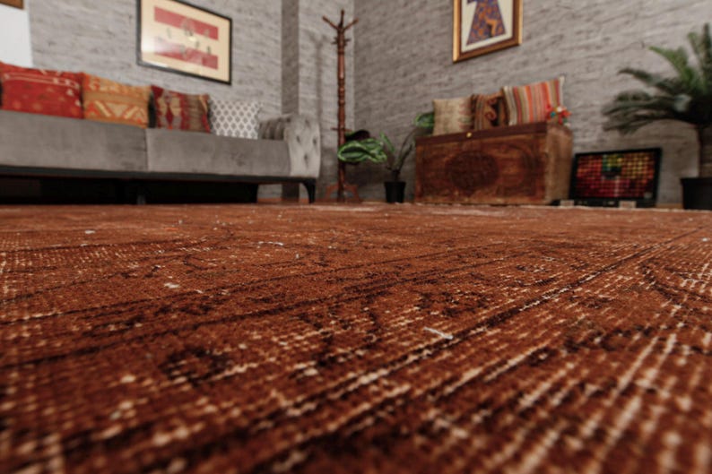 May include: A large, rectangular area rug featuring a deep, rich brown color palette with intricate, faded patterns woven throughout the fabric. The rug has a low-pile texture and covers the floor, displaying a distressed, weathered appearance.