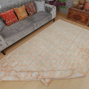 Könnte beinhalten: Ein hellpfirsichfarbener Teppich mit einem weißen Blumenmuster. Der Teppich ist in der Mitte gefaltet und liegt auf einem Holzboden.