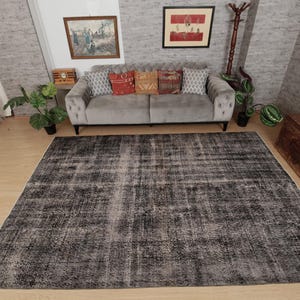 May include: A large rectangular area rug featuring a distressed, faded pattern in shades of charcoal grey, black, and off-white. The rug has a low-pile texture with a weathered appearance, covering a significant portion of the light wood floor.