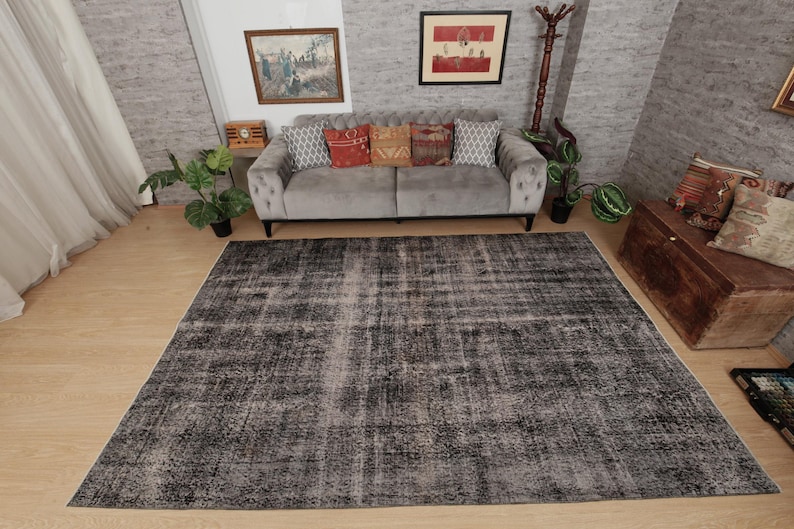 May include: A large rectangular area rug featuring a distressed, faded pattern in shades of charcoal grey, black, and off-white. The rug has a low-pile texture with a weathered appearance, covering a significant portion of the light wood floor.