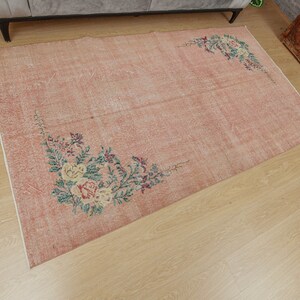 May include: A vintage-style rug with a light pink background and floral designs in shades of green, yellow, and brown. The rug has a distressed look, giving it a unique and charming appeal.