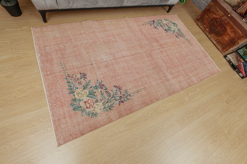May include: A vintage-style rug with a light pink background and floral designs in shades of green, yellow, and brown. The rug has a distressed look, giving it a unique and charming appeal.